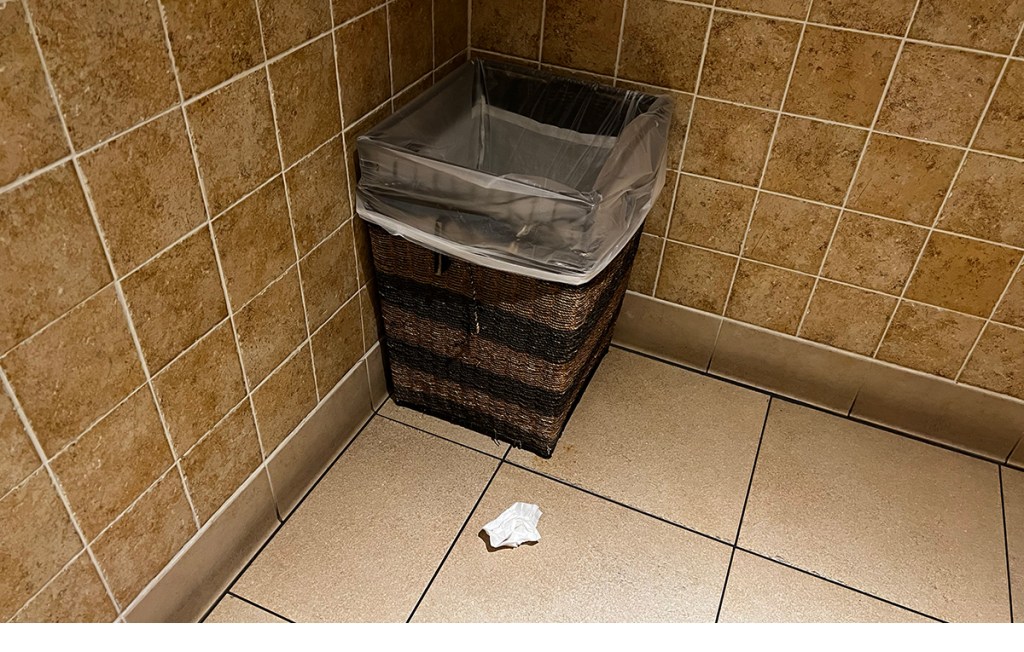 A paper towel on the floor in front of a trash can